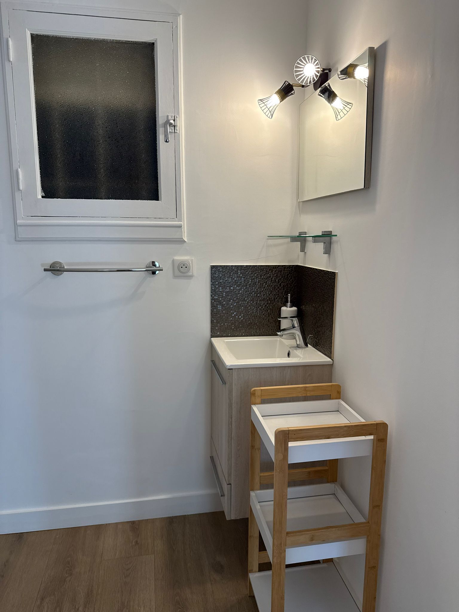 Une salle de bain avec une fenêtre, un miroir, un lavabo et une étagère en bois.