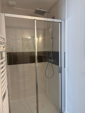 Un box de ducha moderno con puerta de vidrio, un cabezal de ducha de mano y un cabezal de ducha empotrado.