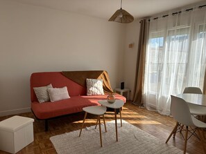 Una sala de estar con un sofá rojo, cojines blancos, una mesita pequeña blanca, un otoman blanco y una silla blanca.
