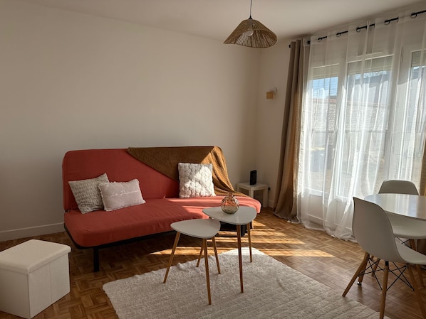 A living room with a red sofa, white cushions, a small white table, a white ottoman, and a white chair.