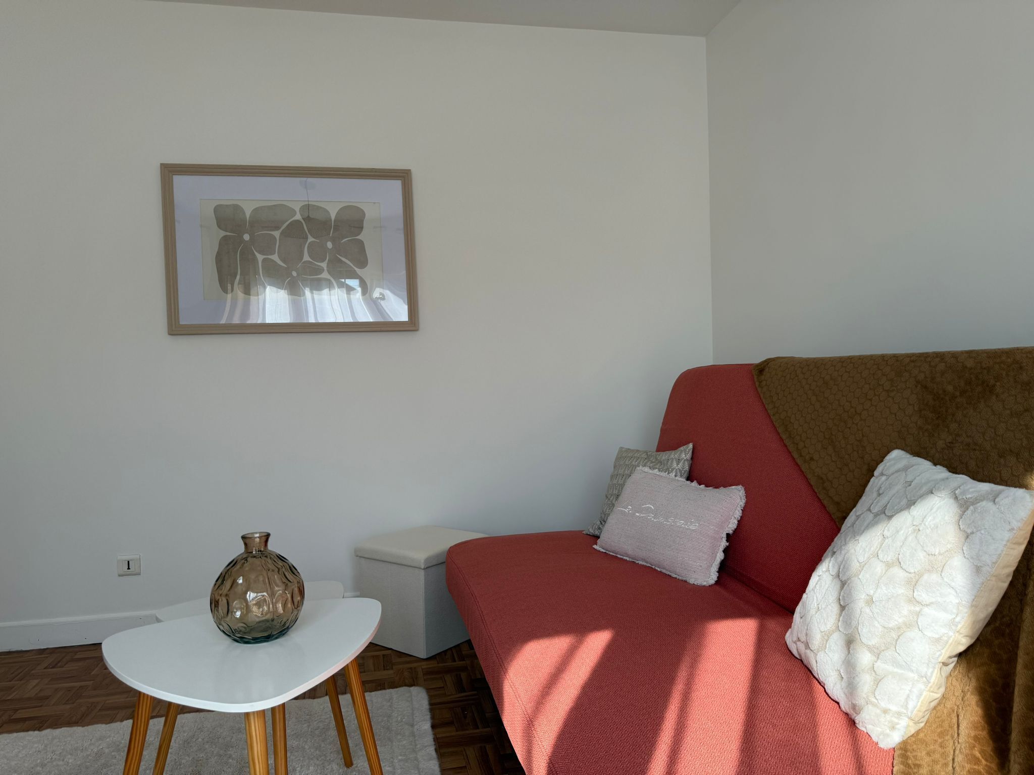 A room with a red sofa, a white table, a vase, and a framed abstract artwork on the wall.