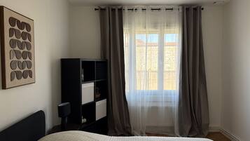 A bedroom with a bed, a black bookshelf, a wall art piece, and a window with sheer curtains.