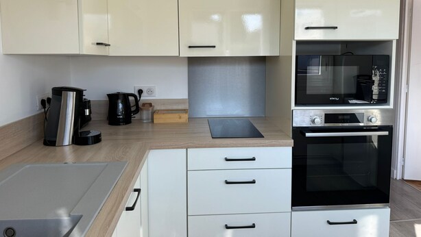 Een moderne keuken met witte kastjes, een inbouwoven en een koffiezetapparaat.