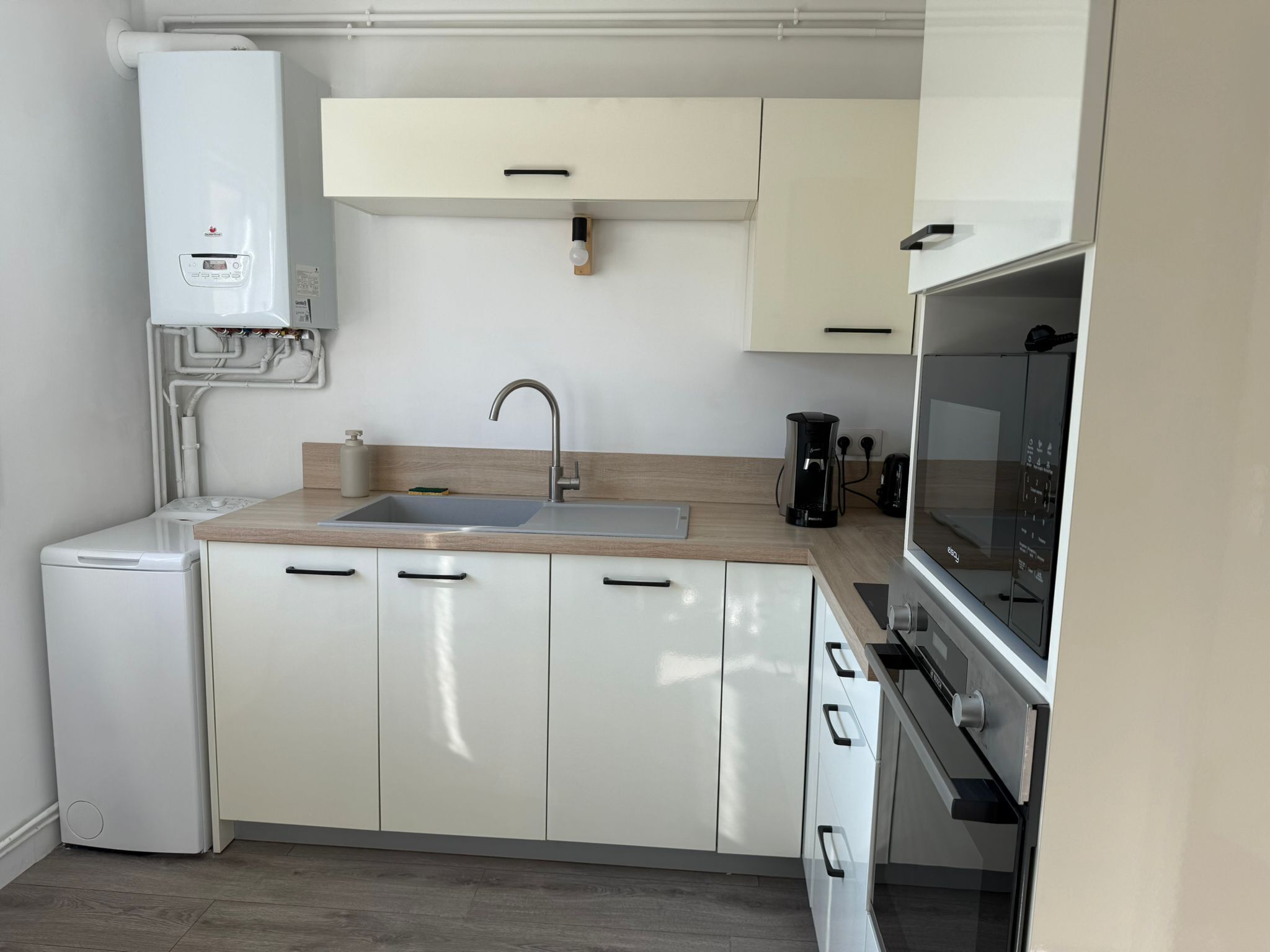 A compact kitchen with white cabinets, a built-in oven, a sink, and a coffee maker.