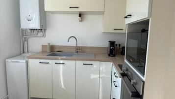 A compact kitchen with white cabinets, a built-in oven, a sink, and a coffee maker.