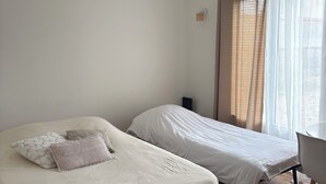 Een kamer met twee bedden, een houten vloer, een hanglamp, een stoel en een raam met gordijnen.