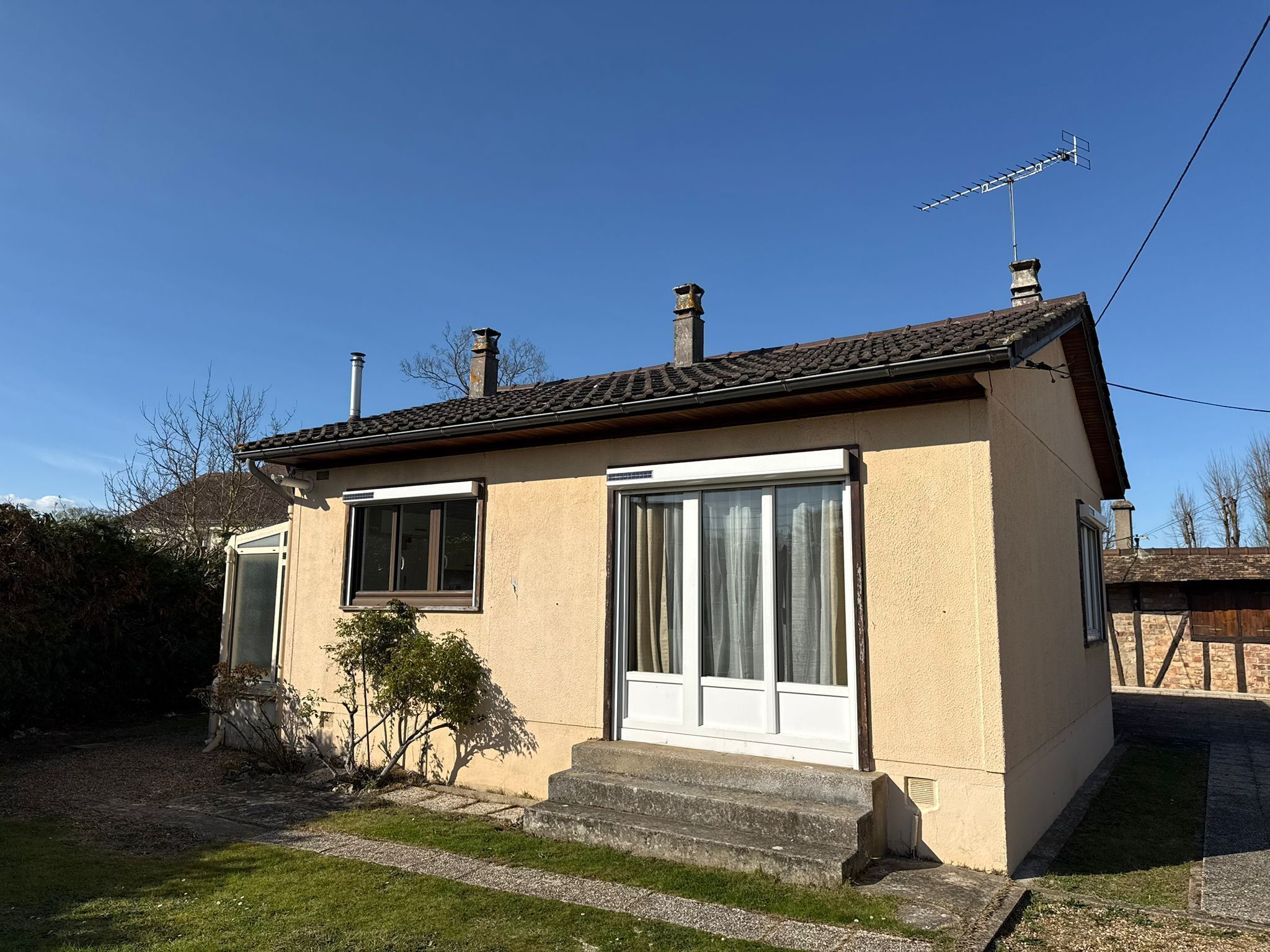 A single-story house with a tiled roof, two windows, a chimney, and a small front yard.