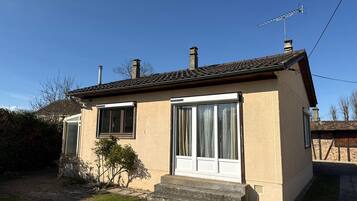 A single-story house with a tiled roof, two windows, a chimney, and a small front yard.