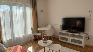 Een woonkamer met een televisie, witte stoelen, een klein tafeltje en een bank.