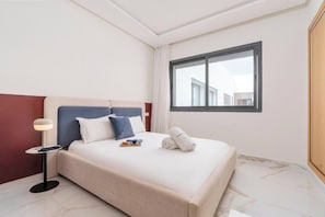 Una habitación de hotel con cama, mesita de noche, ventana y vista a edificios.
