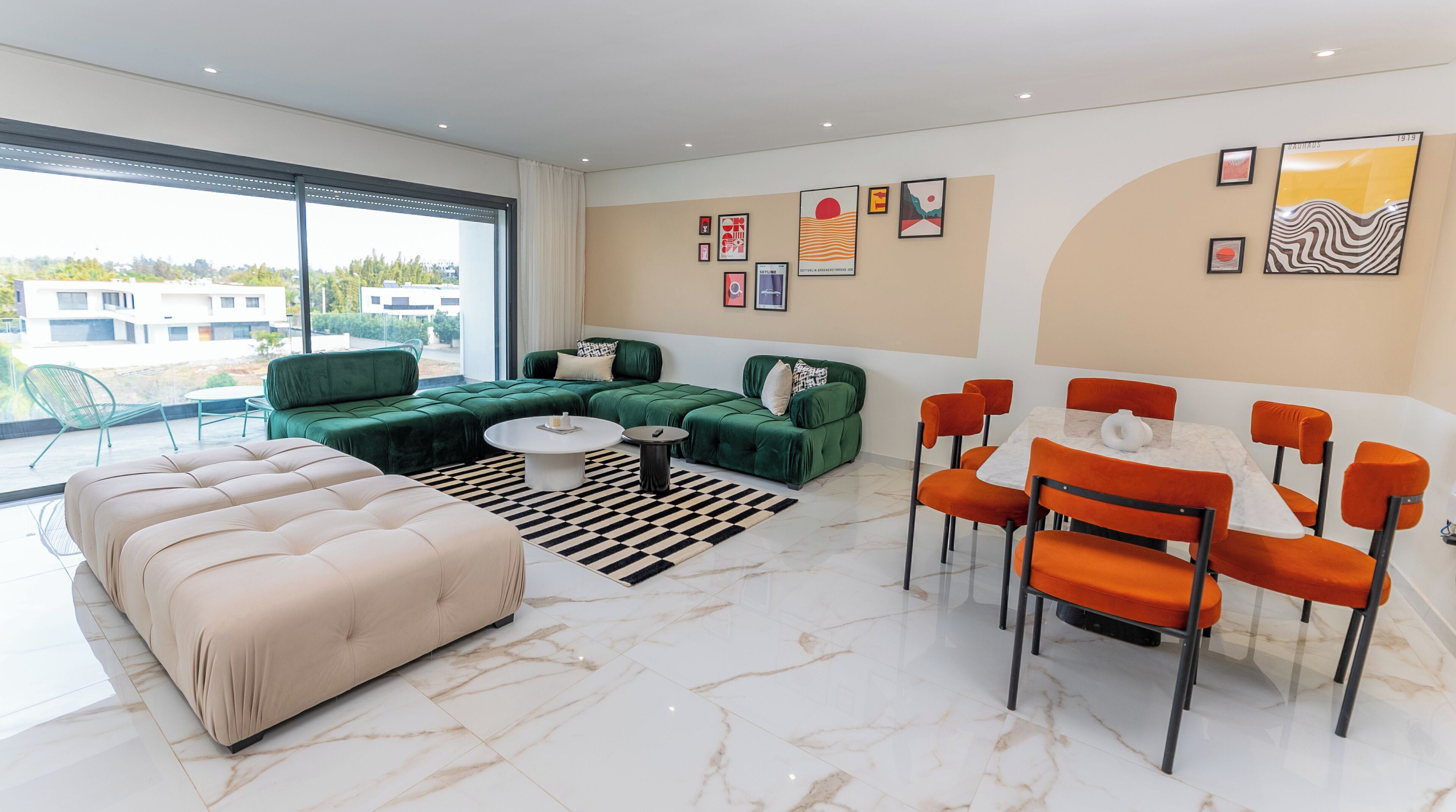 Un salon moderne avec un canapé vert, un pouf beige et un coin repas doté de chaises orange.