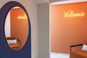 Un intérieur moderne agrémenté d'un néon lumineux affichant le mot « Bienvenue », d'un miroir rond et d'un canapé.