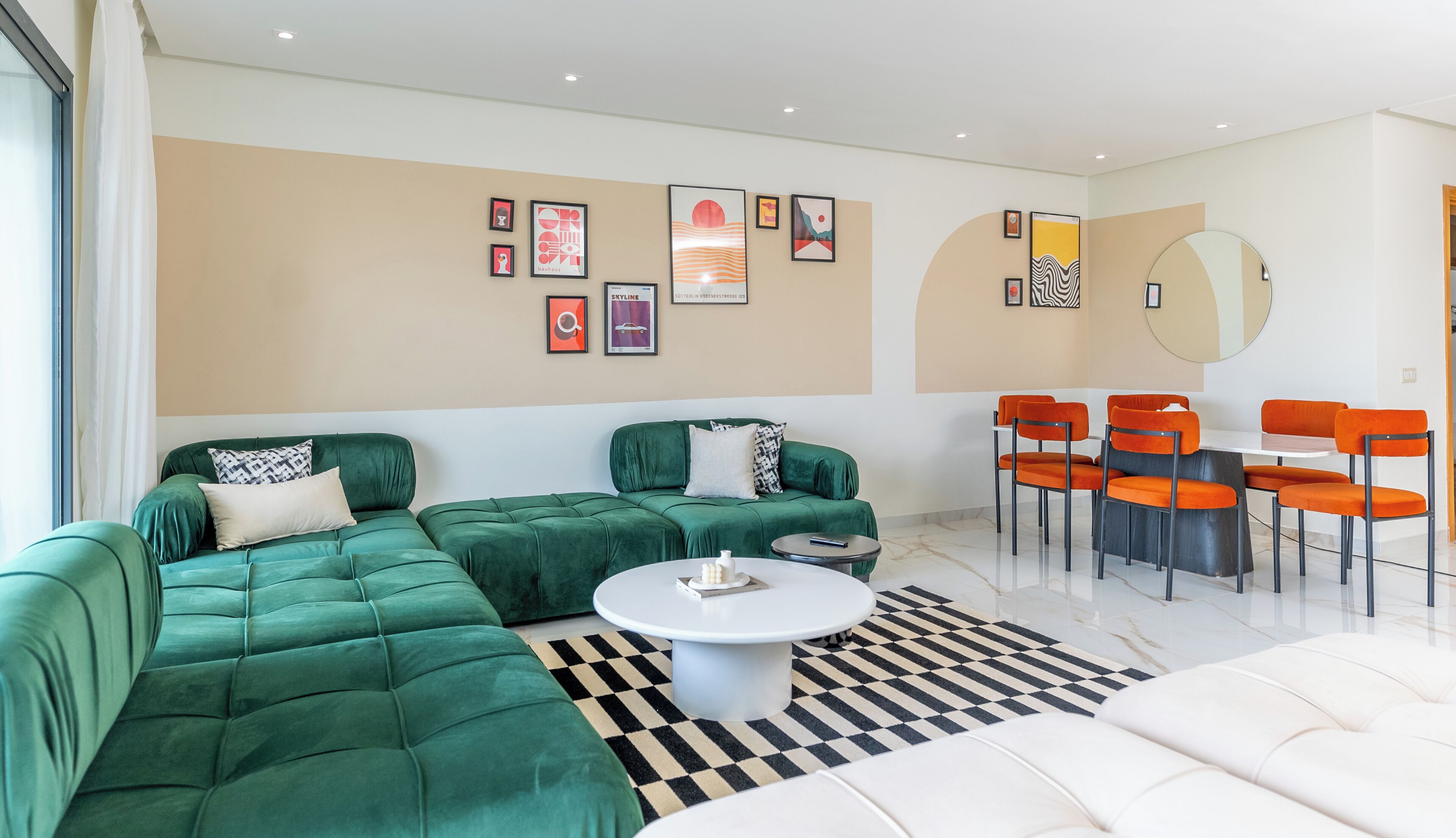 A modern living room with a sectional sofa, a dining table with chairs, and a large mirror.