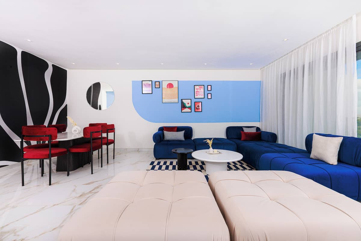 A modern living room with a sectional sofa, a round coffee table, and a dining area with red chairs.
