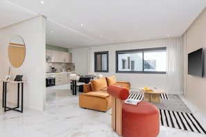 Un salon moderne avec un canapé, un pouf rouge, une table basse et un téléviseur fixé au mur.