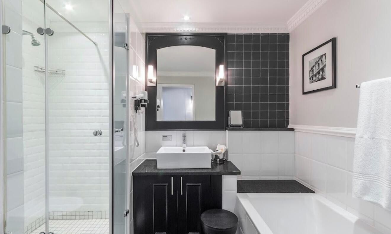 A modern bathroom with a glass shower enclosure, a white sink, a black vanity, a large mirror, and a framed picture on the wall.
