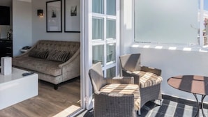 Uma sala de estar moderna com um sofá, cadeiras de vime, uma mesa de centro e uma porta de vidro deslizante que dá para uma varanda.