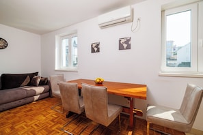 A room with a wooden dining table, four chairs, a sofa, a clock, and two wall-mounted air conditioners. - Studio apartment only 250 m from the sandy beach in Crikvenica (Crikvenica)