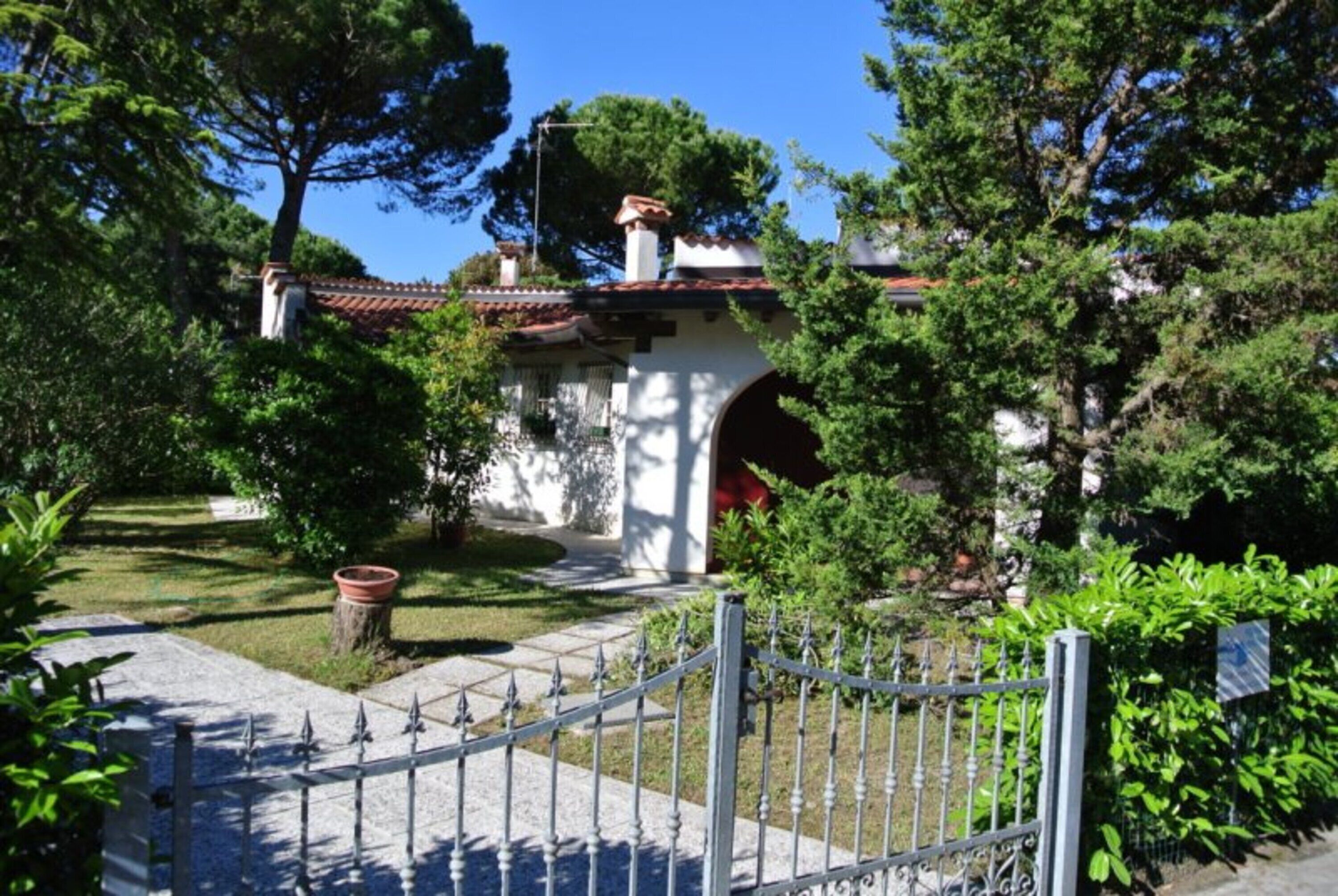 A garden with a white building, a red archway, and a metal fence.