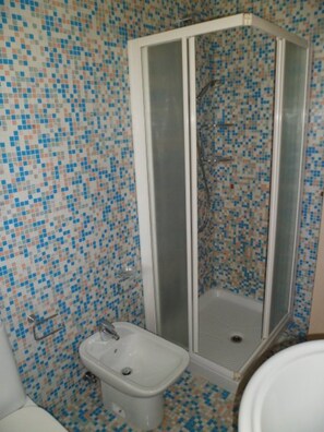 Et badeværelse med bruser, toiletbadekar og vægge beklædt med mosaikfliser.