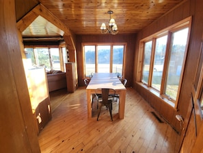 Un interior de madera con una mesa de comedor, sillas, ventanas amplias y una araña.