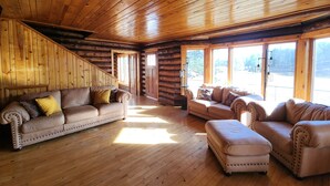 A log cabin interior with a wooden floor, a sofa, an ottoman, and a window with a view. - Private Log Cabin on 20 acres, Across from Custer SP, Close to Mt Rushmore (Custer)