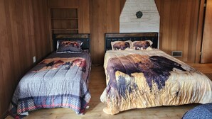 A room with two beds, wooden walls, a stone fireplace, and a ceiling fan. - Private Log Cabin on 20 acres, Across from Custer SP, Close to Mt Rushmore (Custer)