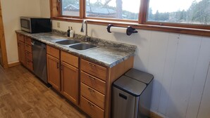 A kitchen with wooden cabinets, a stainless steel sink, a microwave, and a window with a view of trees. - Private Log Cabin on 20 acres, Across from Custer SP, Close to Mt Rushmore (Custer)