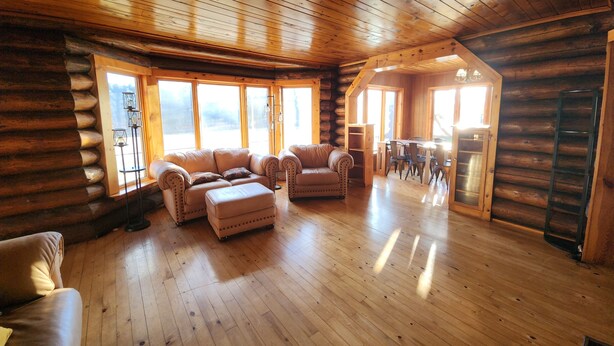 A log cabin interior with a wooden floor, leather sofas, a dining area, and large windows. - Private Log Cabin on 20 acres, Across from Custer SP, Close to Mt Rushmore (Custer)