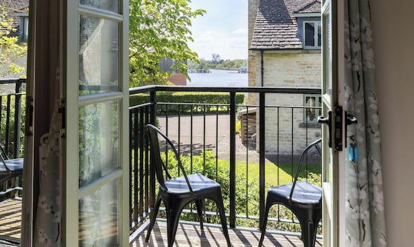 An open door to a balcony with a view of a lake, two chairs, and a stone wall. - Mill Village 43, Dragonfly - Spa & Swimming Pool Access, Watersports & Pet Friendly, Sleeps 6 (Somerford Keynes)