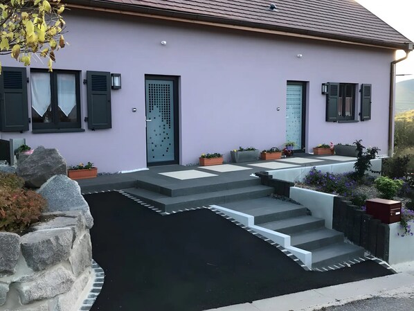 Une maison moderne avec une façade grise, un escalier menant Ă une porte et des plantes en pot disposĂ©es autour de lâentrĂ©e.