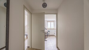 A hallway leading to a bedroom with a bed, a desk, and a chair.