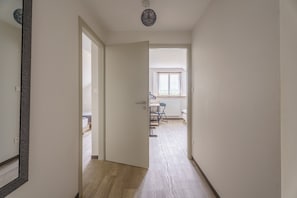 A hallway leading to a bedroom with a bed, a desk, and a chair.