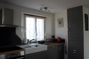 Une cuisine moderne dotĂ©e dâune hotte en acier inoxydable, dâun four encastrĂ©, dâun Ă©vier et dâune fenĂȘtre avec des rideaux.