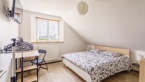 A bedroom with a bed, a desk, a chair, a radiator, a window, and a ceiling light fixture.