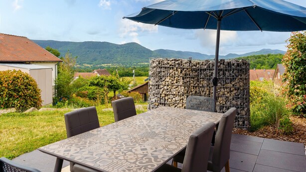 An outdoor patio with a table and chairs, a blue umbrella, and a stone wall.