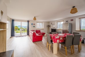 A spacious living area with a red sofa, a dining table with chairs, and a kitchen area.