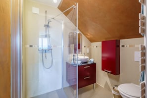 A modern bathroom with a glass shower enclosure, a white sink, and a red cabinet.
