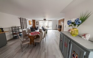 Un salon moderne comprenant un coin repas, une cuisine et une vue dégagée grâce aux portes vitrées.