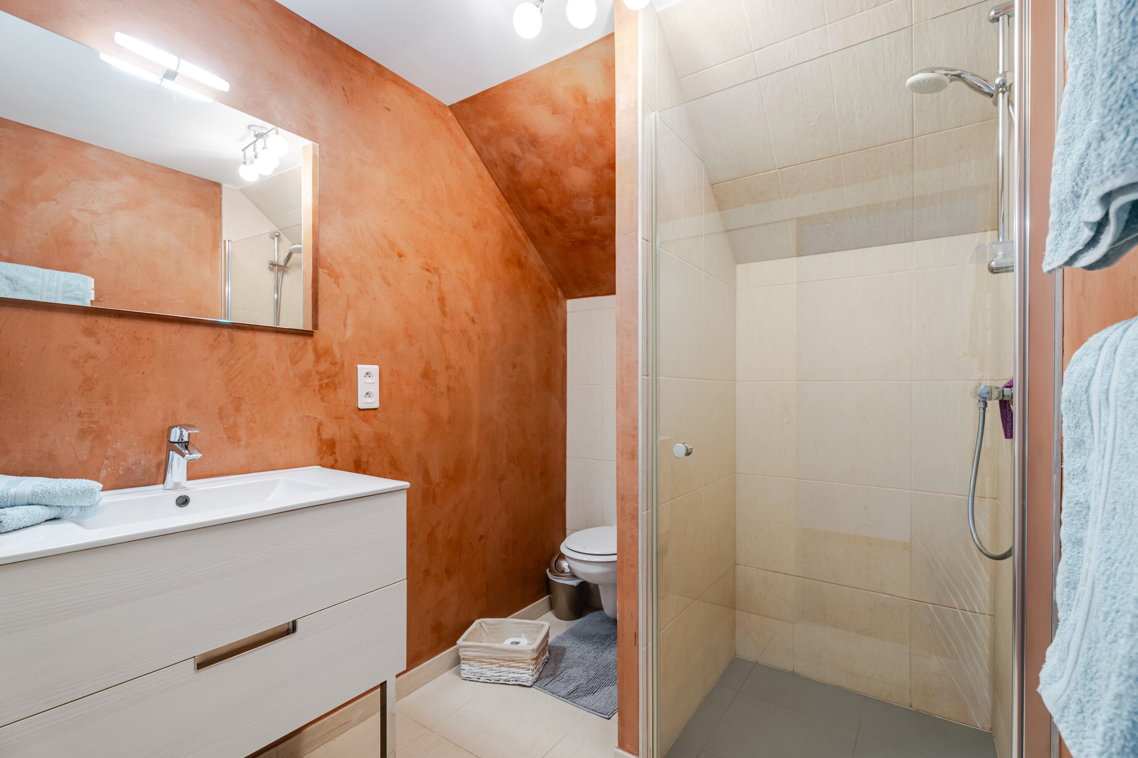 Et badeværelse med vask, spejl, bruser og toilet.