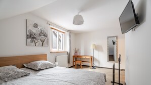 Een slaapkamer met een bed, een bureau, een stoel, een televisie en een raam met gordijnen.
