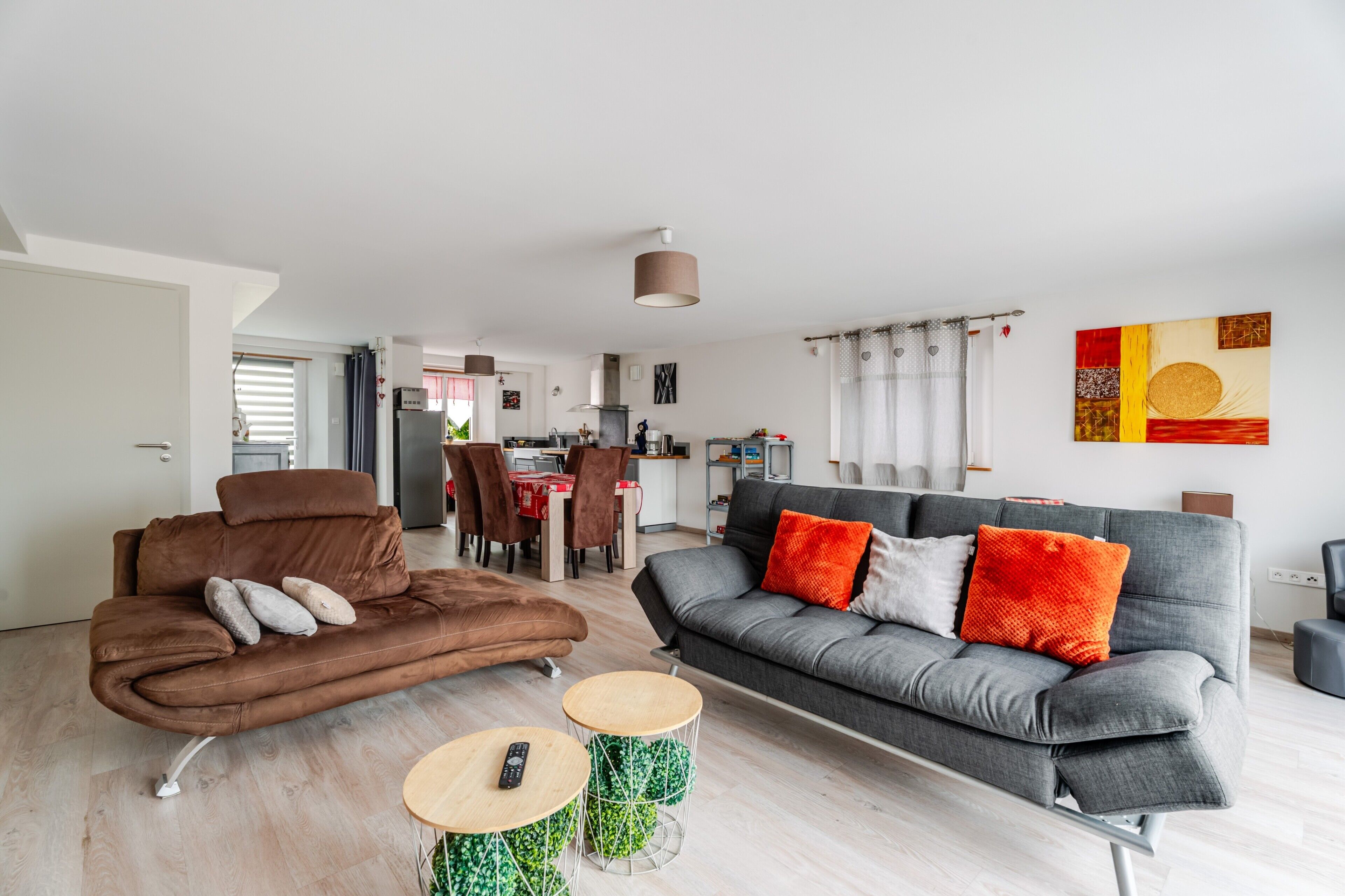 A modern living room with a brown sofa, grey sofa, and two round wooden tables.