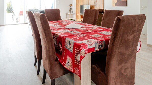 Een eethoek met een tafel bedekt met een rode tafelkleed, omringd door zes bruine stoelen.