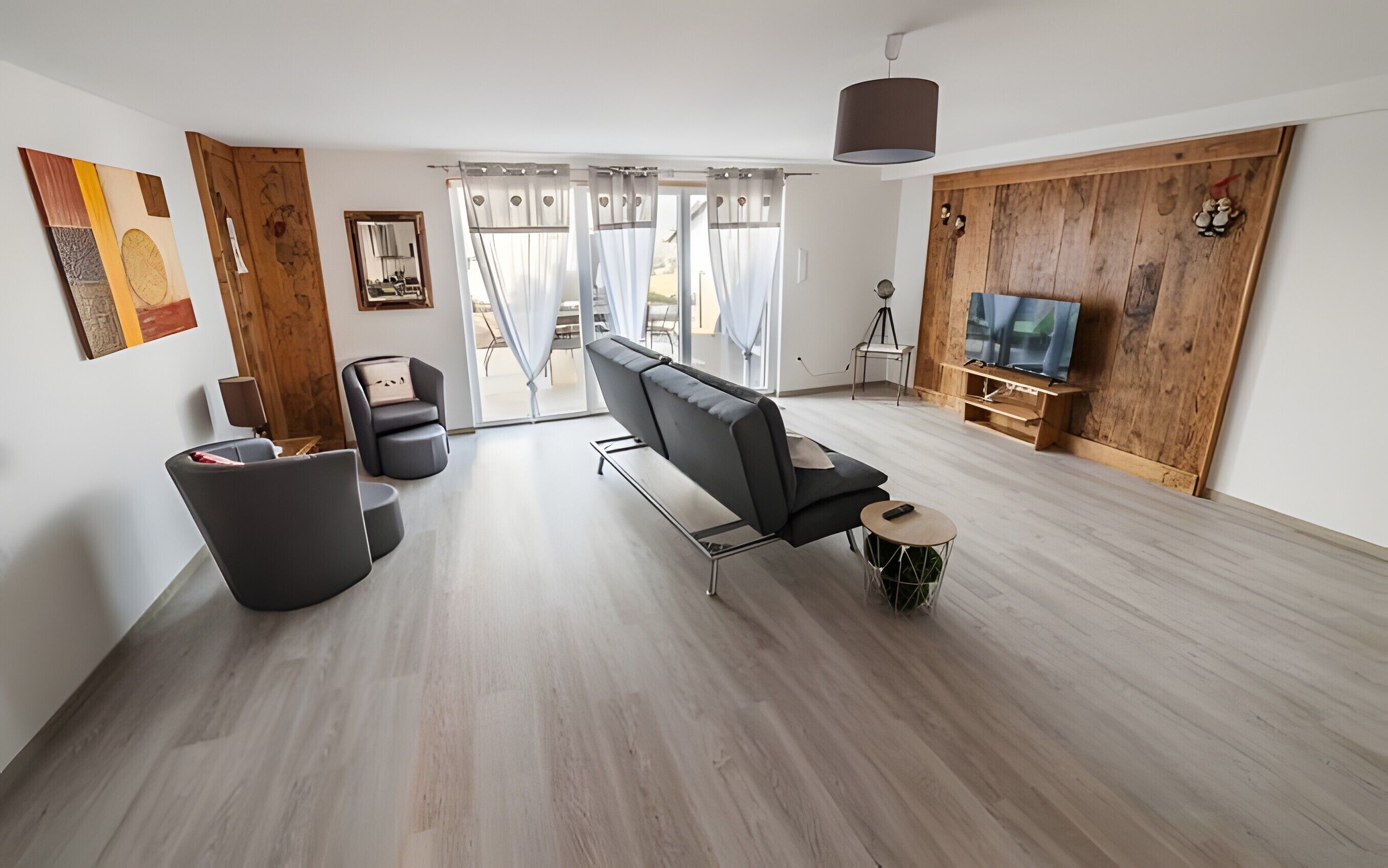 A modern living room with a sofa, a TV, and a wooden wall.. Gîte aux deux hameaux (1) – Mountain Retreat with Panoramic Views