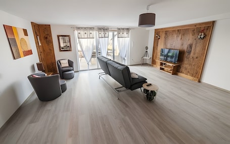 A modern living room with a sofa, a TV, and a wooden wall.. Gîte aux deux hameaux (1) – Mountain Retreat with Panoramic Views