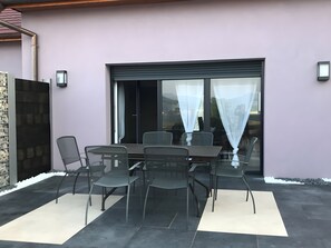Une terrasse avec une table et des chaises, une porte-fenêtre coulissante et un mur en pierre.
