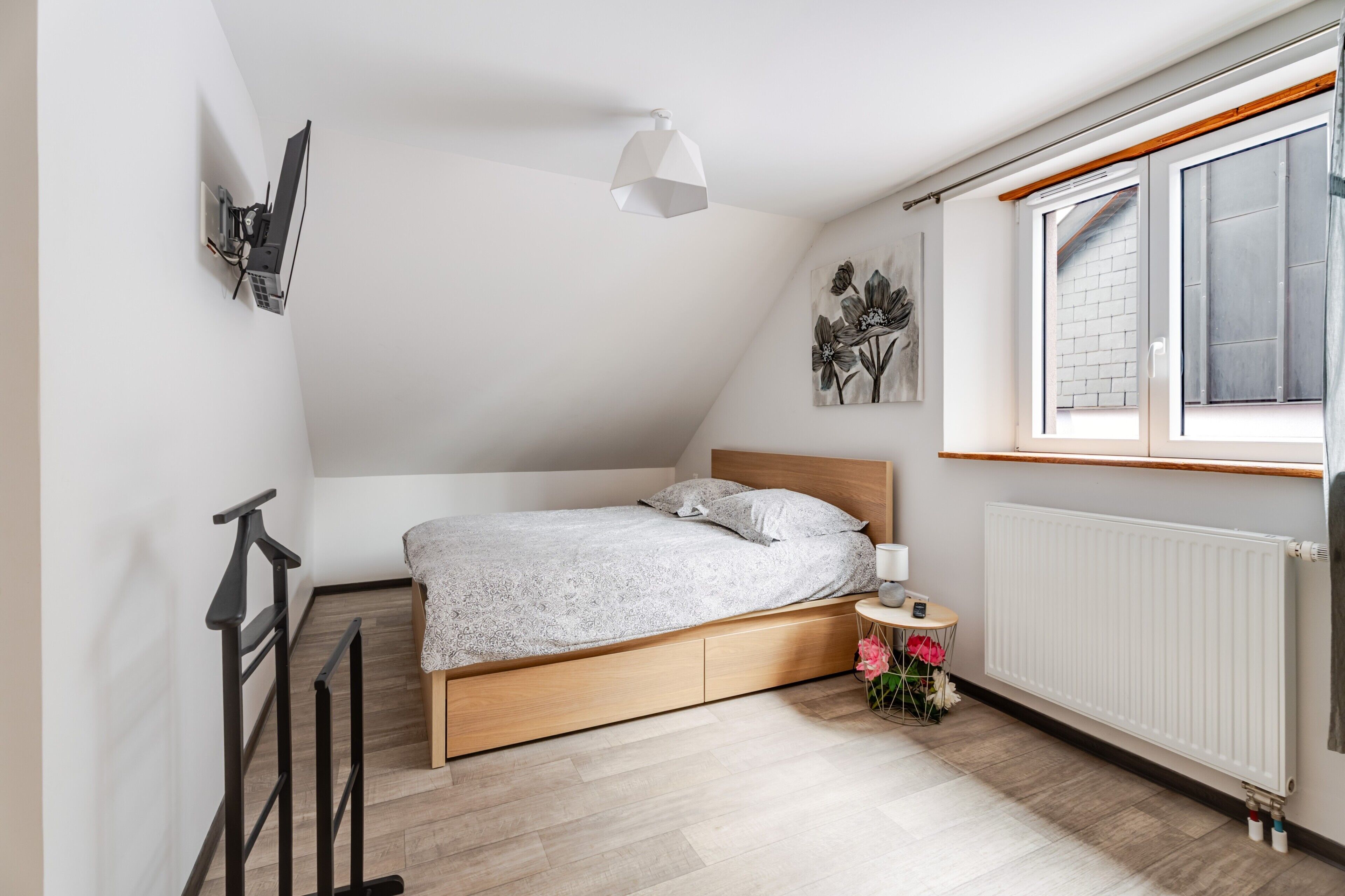 Et soveværelse med seng, en radiator, et vindue og et lille bord med lampe.
