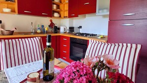 A modern kitchen with red cabinets, a dining area with striped cushions, and a table with a bottle and flowers. - Charming Historic House in Provincia di Cuneo, Italia (Mombarcaro)