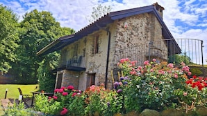 A rustic stone building with a balcony, surrounded by a garden with various flowers. - Charming Historic House in Provincia di Cuneo, Italia (Mombarcaro)