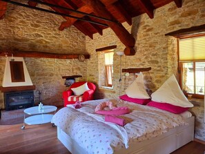 A bedroom with a stone wall, a fireplace, a bed with pink and white bedding, a red chair, and a small round table. - Charming Historic House in Provincia di Cuneo, Italia (Mombarcaro)